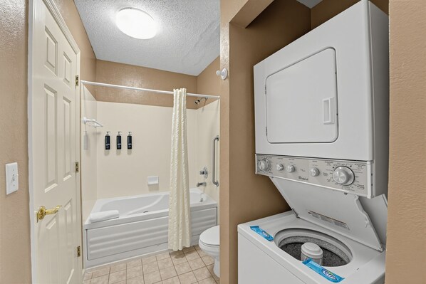 A bathroom with a bathtub, toilet, and a front-loading washing machine. - Cozy Pigeon Forge Stay w/ Full Kitchen + Pools (Pigeon Forge)