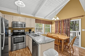 A kitchen with stainless steel appliances, a granite countertop, and a dining area with wooden chairs. - Mountain Cottage with Loft & Private Balcony (Pigeon Forge)