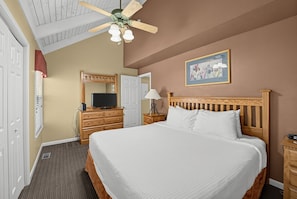 A hotel room with a large bed, a wooden headboard, a ceiling fan, a television on a dresser, and a painting on the wall. - Mountain Cottage with Loft & Private Balcony (Pigeon Forge)