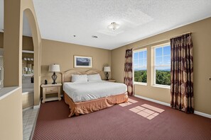 A hotel room with a large bed, two bedside tables, a nightstand, a window with curtains, and a view of the outdoors. - Spacious Condo with Fireplace & Full Kitchen (Pigeon Forge)