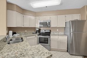 A kitchen with white cabinets, a stainless steel refrigerator, a built-in microwave, a double oven, and a granite countertop. - Spacious Condo with Fireplace & Full Kitchen (Pigeon Forge)