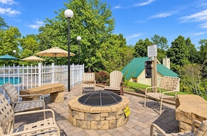 An outdoor patio area with stone seating, a fire pit, and umbrellas. - Spacious Condo with Fireplace & Full Kitchen (Pigeon Forge)