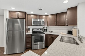 A modern kitchen with stainless steel appliances, wooden cabinets, and a granite countertop. - Renovated Mountain View Condo with Fireplace (Pigeon Forge)