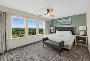 A hotel room with a large bed, a desk, a chair, a ceiling fan, and a window with a view of trees. - Renovated Mountain View Condo with Fireplace (Pigeon Forge)