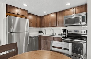 A kitchen with stainless steel appliances, wooden cabinets, a sink, and a dining area with a table and chairs. - Pigeon Forge Renovated Condo w/ Private Balcony (Pigeon Forge)