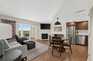 A modern living room with a fireplace, a dining area with a round table, and a kitchen with stainless steel appliances. - Pigeon Forge Renovated Condo w/ Private Balcony (Pigeon Forge)