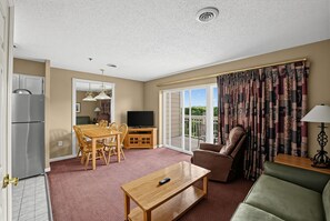 A hotel room with a dining area, a sofa, a recliner, a TV, and a balcony with curtains. - Mountain View Condo Near Dollywood | Pools Onsite! (Pigeon Forge)