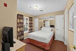 A hotel room with a bed, a desk with a television, a window with curtains, and a door. - Mountain View Condo Near Dollywood | Pools Onsite! (Pigeon Forge)