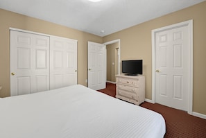 A bedroom with a large bed, two white doors, a dresser with a television, and a carpeted floor. - Mountain View Condo with Fireplace & Balcony (Pigeon Forge)