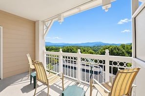 A balcony with a view of a mountain range, two striped chairs, and a table. - Mountain View Condo with Fireplace & Balcony (Pigeon Forge)