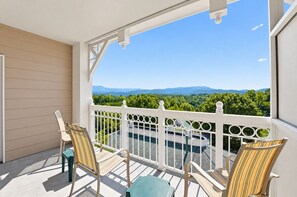 A balcony with a view of mountains and greenery, furnished with striped chairs and a table. - Mountain View Condo w/ Balcony | Near Dollywood! (Pigeon Forge)