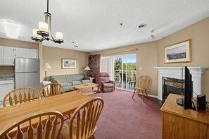 A spacious living area with a dining table, chairs, a sofa, a fireplace, and a balcony with a view. - Mountain View Condo w/ Balcony | Near Dollywood! (Pigeon Forge)