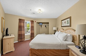 A hotel room with a bed, bedside tables, a desk, a television, and a window with curtains. - Mountain View Condo w/ Balcony | Near Dollywood! (Pigeon Forge)