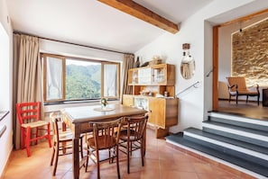 A dining area with a wooden table and chairs, a view of the outdoors, a stone wall, and a staircase. - Authentic apartment in medieval Apricale (Apricale)