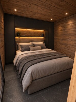 A modern bedroom with a large bed, dark wood paneling, and recessed lighting. - Ruka Timber Chalets  (Kuusamo)