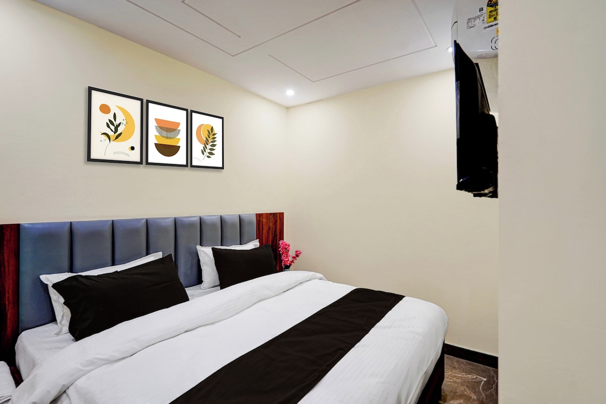 A hotel room with a bed, a headboard, a flat-screen TV mounted on the wall, and three framed artworks above the bed.