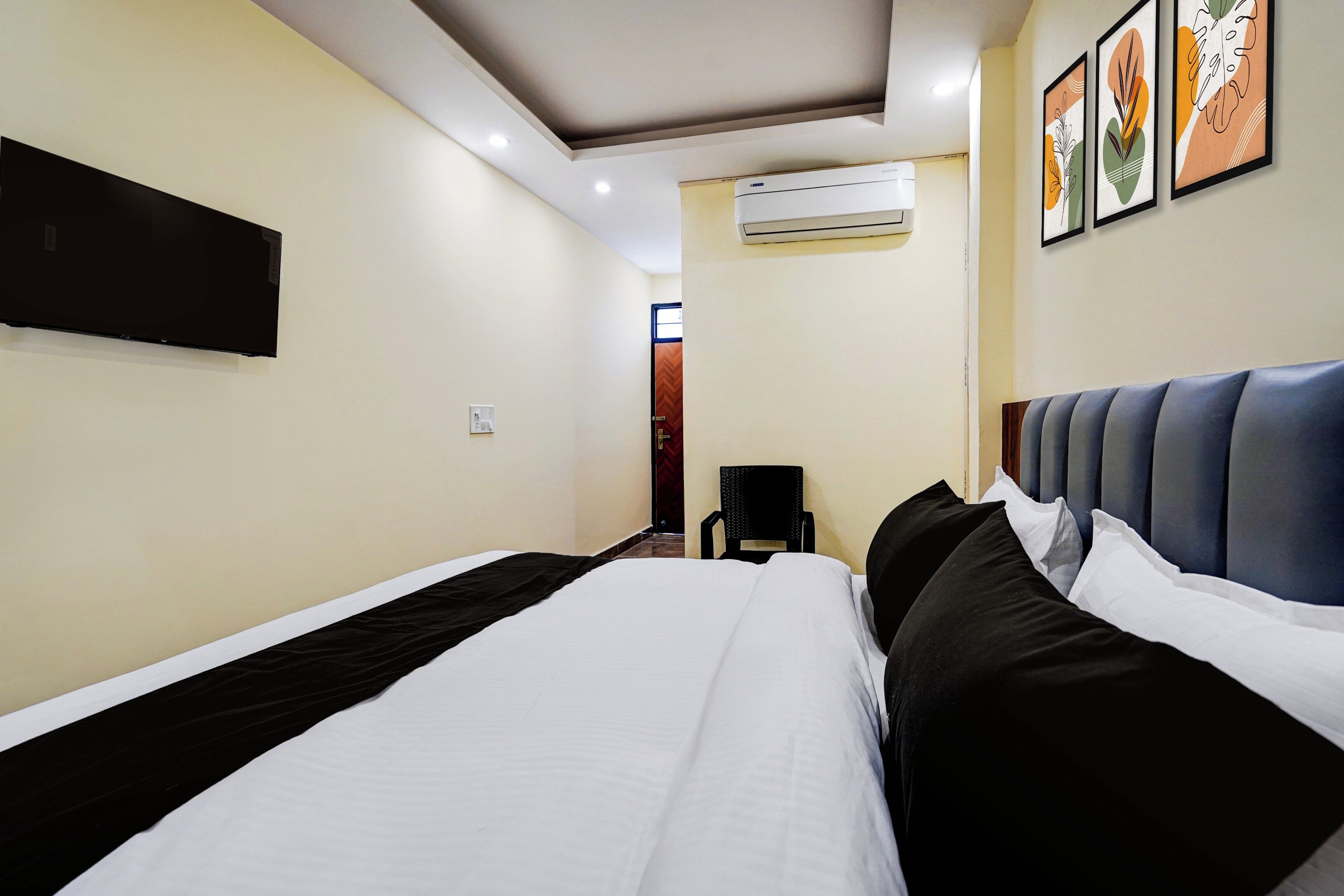 Habitación de hotel con cama, televisor de pantalla plana en la pared, equipo de aire acondicionado y una obra de arte enmarcada sobre la cama.