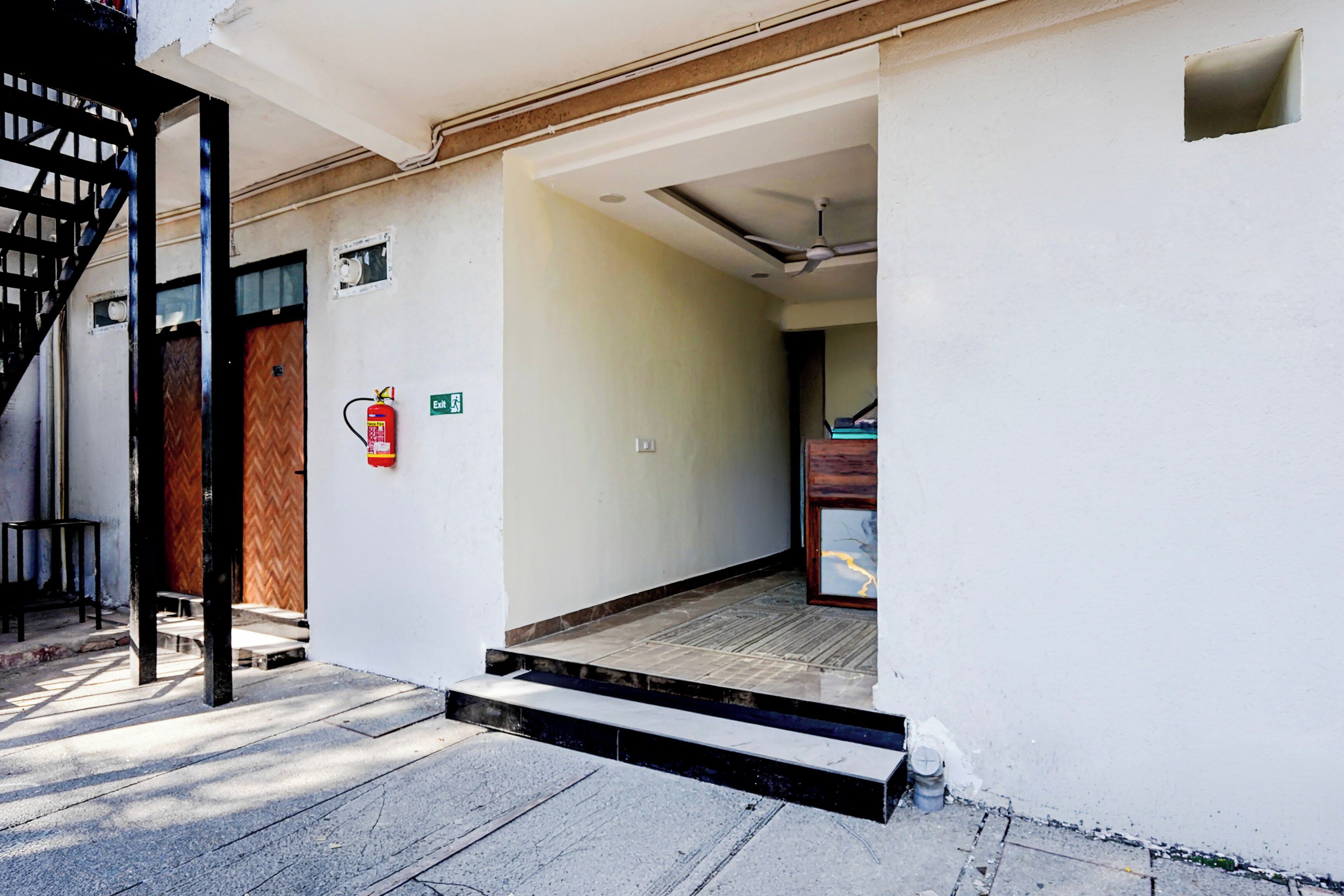Una entrada de edificio con un extintor en la pared, una puerta con diseño de espiga y un escalón que da acceso al interior.