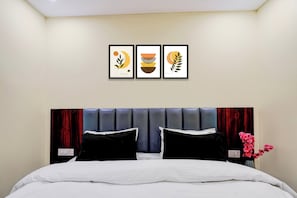 A hotel room with a bed, two black pillows, a headboard, and three framed artworks on the wall. - Super Hotel O Survey Chowk Bus Terminal (Dehradun)