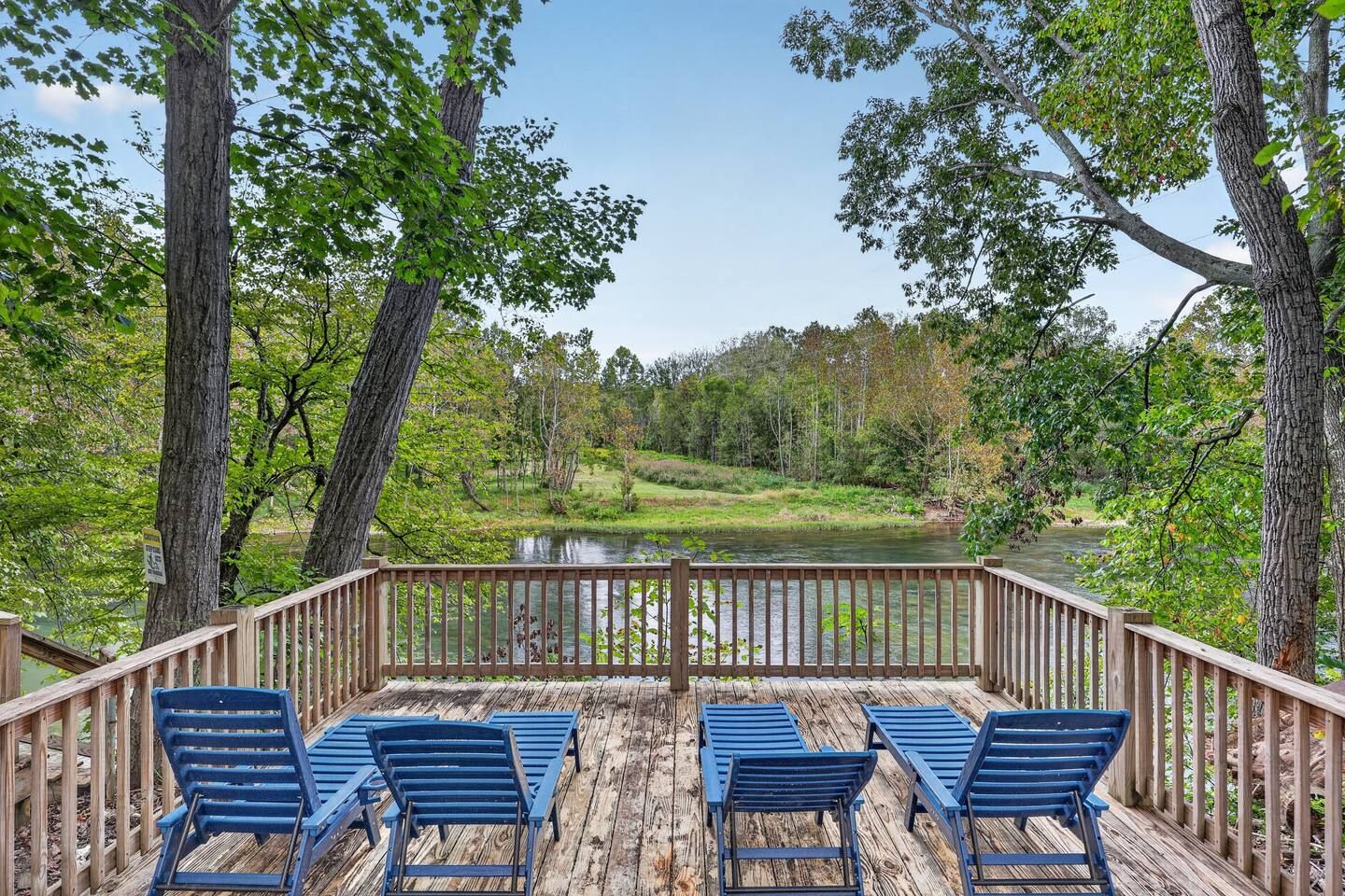 A wooden deck with blue chairs overlooking a river and forest.