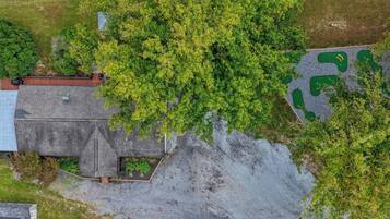 An aerial view of a property with a large tree, a building with a sloped roof, and a gravel area with green shapes.