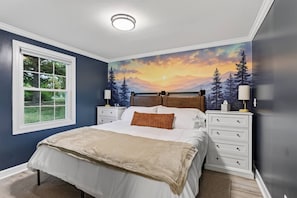A bedroom with a bed, a nightstand, a lamp, a window, and a mural on the wall. - Riverfront Cabin w/ 9-Hole Mini Golf + Hot Tub (Shenandoah)