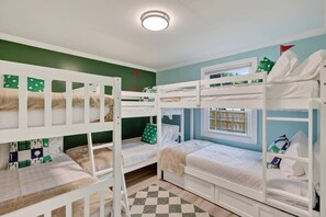Une chambre avec un lit superposé, deux lits, une fenêtre et un tapis à carreaux.