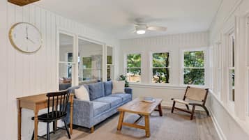 A room with a wooden table, a blue sofa, a wooden chair, and a clock on the wall.