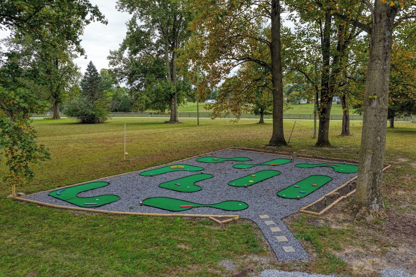 An outdoor mini-golf course with multiple holes, surrounded by trees and a grassy area.