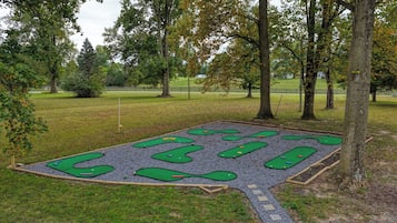 An outdoor mini-golf course with multiple holes, surrounded by trees and a grassy area.