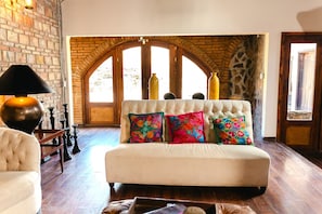 A room with a white sofa, colorful pillows, a lamp, and a brick wall. - Private Cabin 1 - Long Stay Hacienda Cuatro Milpas (El Sauzal)