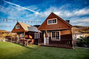 Two wooden cabins with a grassy yard and a string of lights. - Private Cabin 1 - Long Stay Hacienda Cuatro Milpas (El Sauzal)