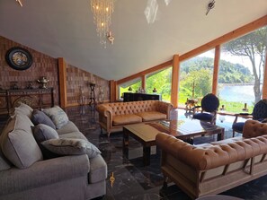 A spacious living room with a large window, a fireplace, and a view of a lake. - New Listing (Puerto montt)