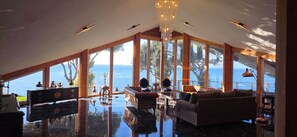 Un amplio salón con un gran ventanal con vista a una masa de agua, un candelabro y una decoración de estilo moderno.
