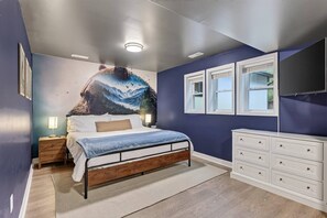Un dormitorio con cama, cómoda, mesita de noche y un mural en la pared.