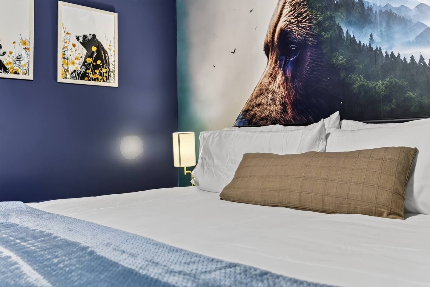 A bedroom with a bed, pillows, a nightstand with a lamp, and wall art.