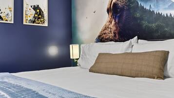 Un dormitorio con cama, almohadas, una mesita de noche con lámpara y decoración en la pared.