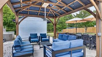 Un espacio de estar techado al aire libre con una estructura de pérgola, muebles de exterior y una parrilla de barbacoa.