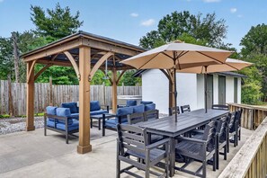 An outdoor patio with a wooden pergola, blue cushioned seating, a dining table, and a large umbrella. - Riverfront Cabin - Pickleball, Hot Tub, Game Room (Shenandoah)