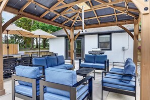 Un patio exterior con una zona de estar cubierta, una parrilla para barbacoa y una terraza de madera.