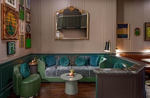 Una habitación con un sofá verde, una mesa de centro redonda y un espejo con marco dorado.