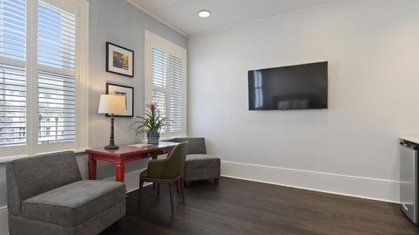 Una habitación con una televisión de pantalla plana montada en la pared, una mesa de comedor con sillas y una ventana con persianas.