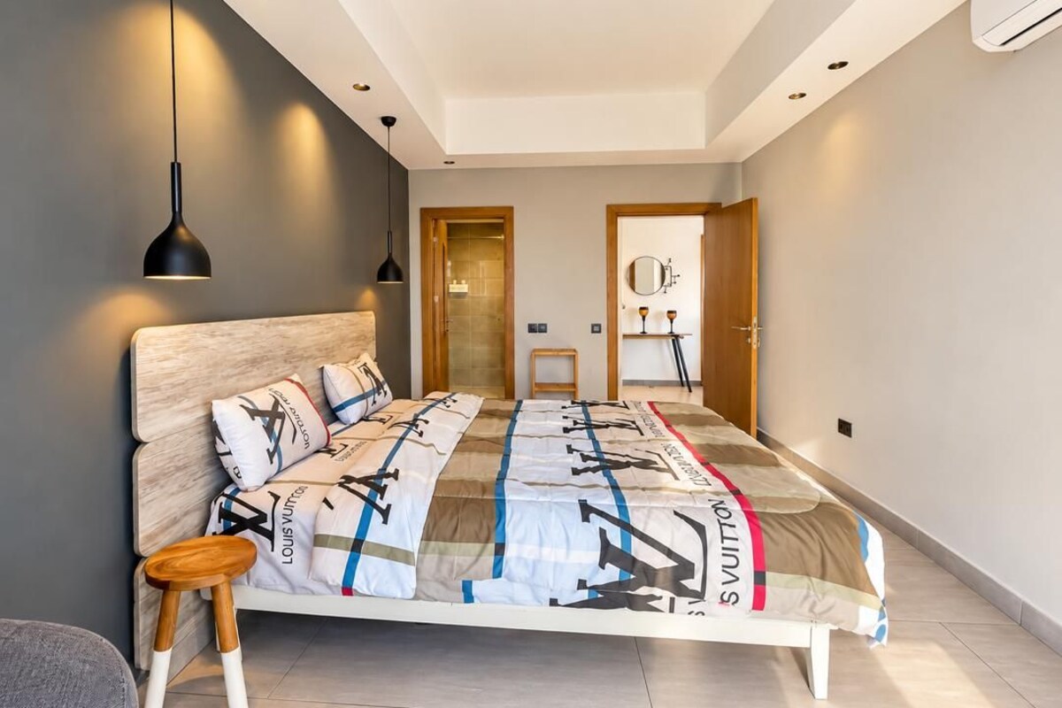 Une chambre à coucher moderne avec un grand lit, une tête de lit en bois, une table de chevet et un luminaire suspendu.
