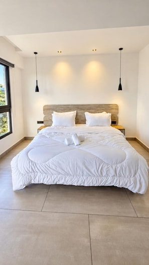 Une chambre à coucher moderne avec un grand lit, deux tables de chevet et une tête de lit dotée d’un éclairage intégré.
