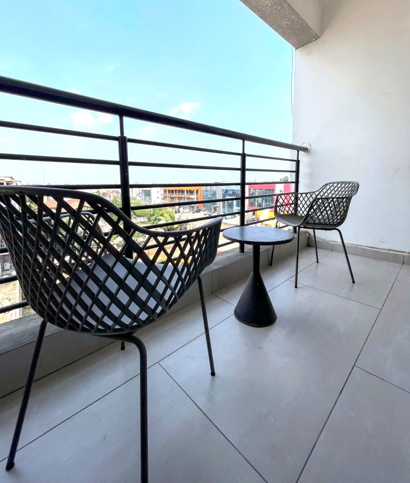 Een balkon met twee stoelen en een tafeltje, met uitzicht op een stadsgezicht.