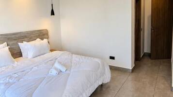 Habitación de hotel moderna con una cama grande, cabecera de madera, lámpara colgante y puerta de madera.