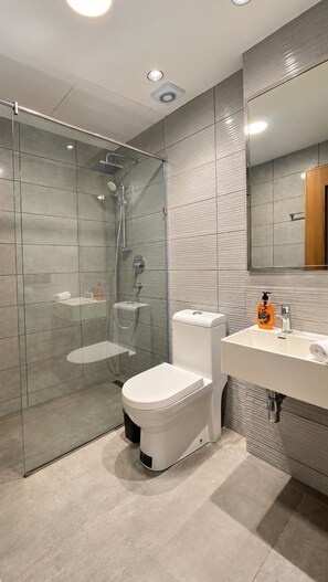 Une salle de bain moderne avec une douche à parois de verre, des toilettes blanches, un lavabo avec un miroir et des murs carrelés.