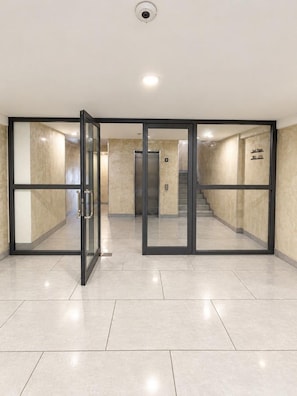 Un interior moderno con entrada por puerta de cristal, un ascensor a la vista y suelo de baldosas.