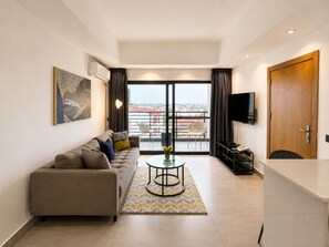 Una sala moderna con sofá, mesa de centro y televisor. Cuenta con un balcón con vista a la ciudad.