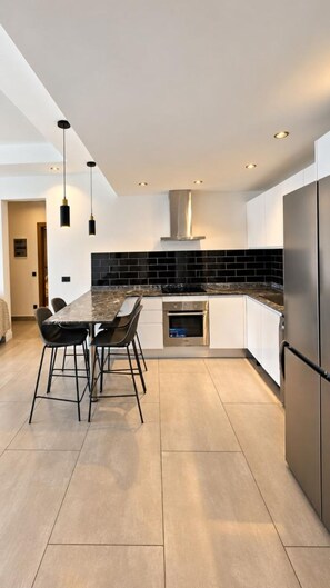Cocina moderna con encimera de mármol, electrodomésticos de acero inoxidable y salpicadero de azulejos negros.